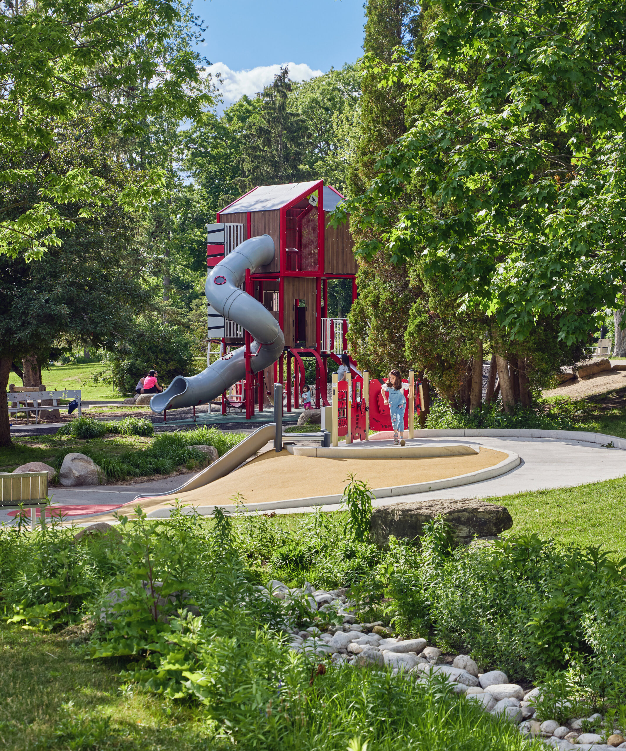 Image of a tall play structure surrounded by trees. Father and small child in foreground.