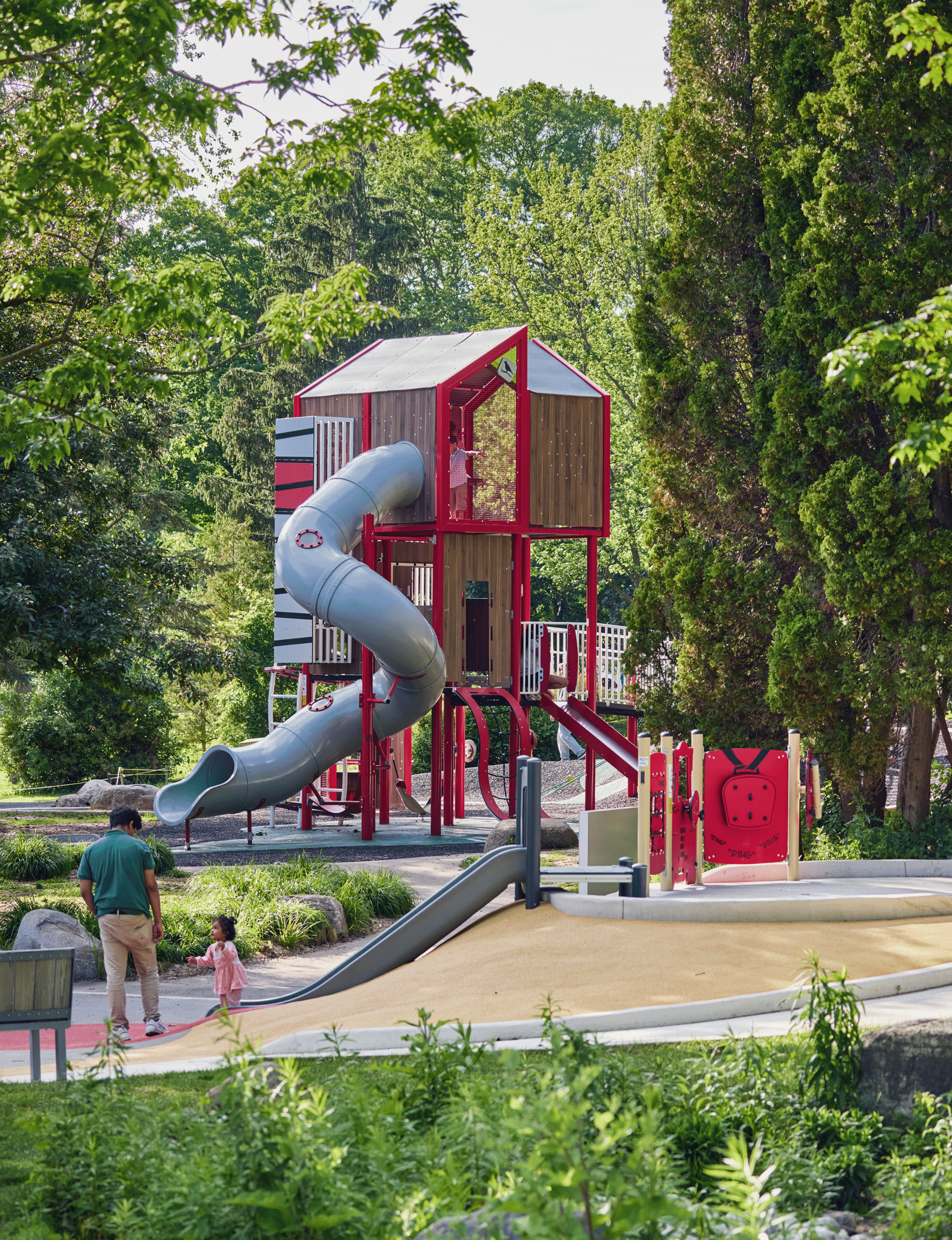 Image of a tall play structure surrounded by trees. Father and small child in foreground.